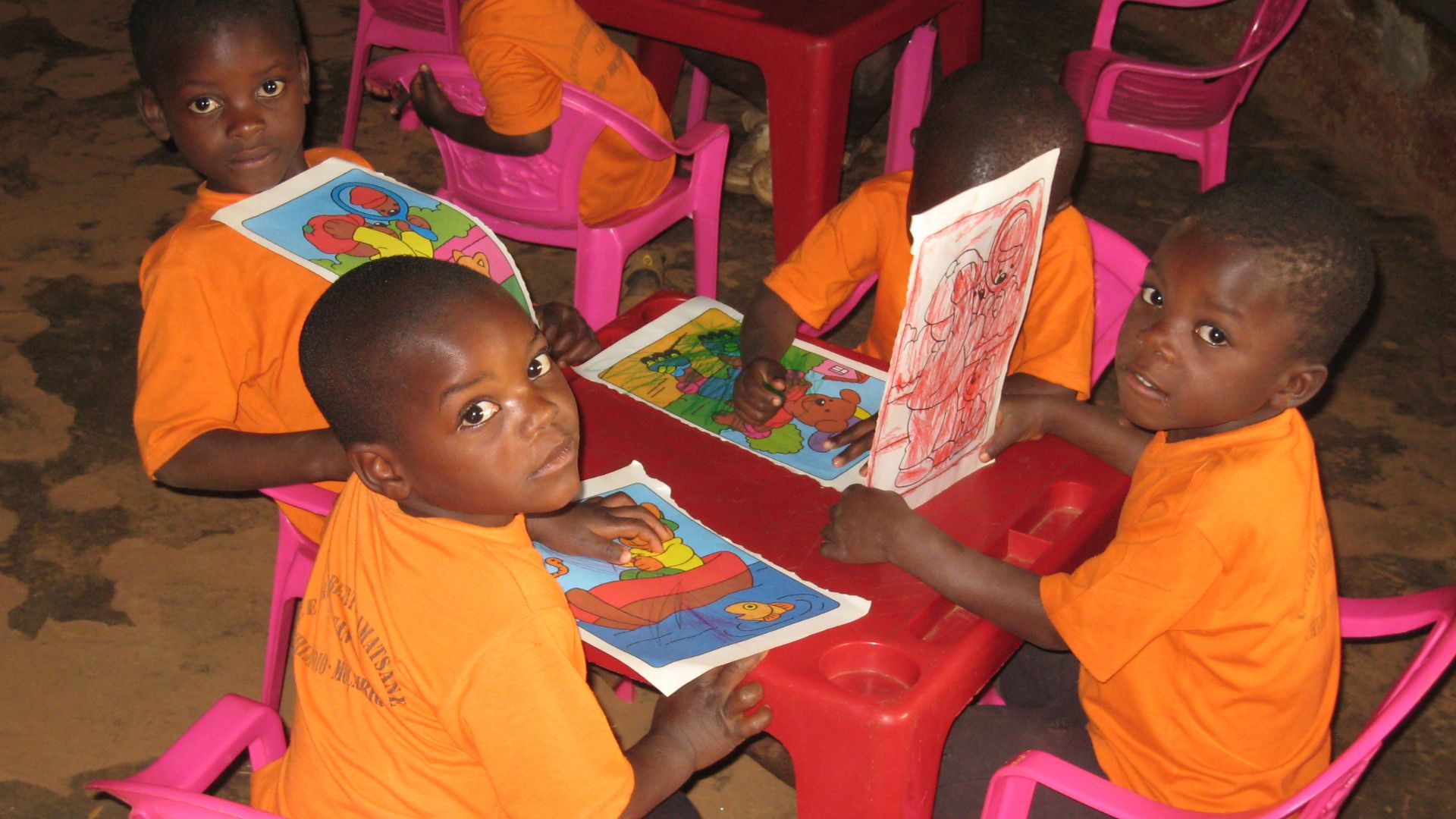 Mosambikilaisia esikoululaisia istumassa pöydän ääressä. Lapset esittelevät piirustuksiaan.